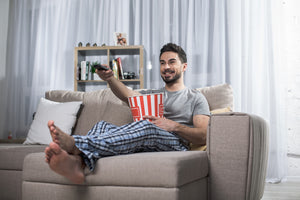 Man on sofa with popcorn recovering from vasectomy with ice pack.